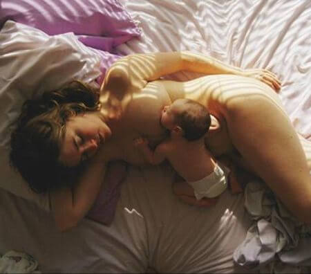 Mamma som ligger i sängen med bebis.