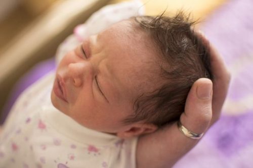 En hand håller den nyfödda bebisens huvud.