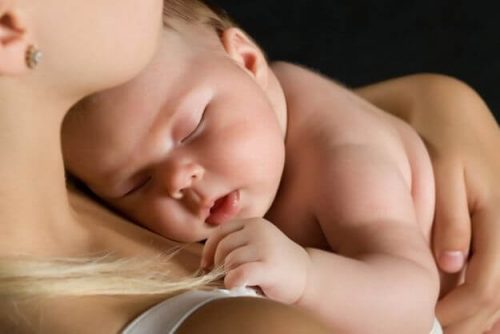 En bebis sover i sin mammas famn.