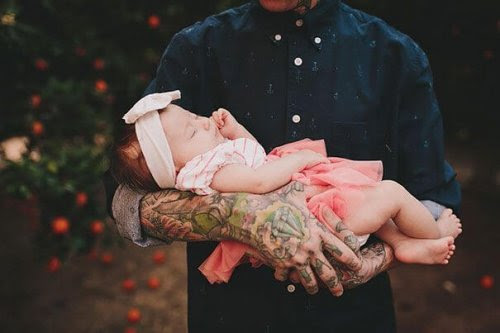 Man med tatuerade armar håller spädbarn i famnen