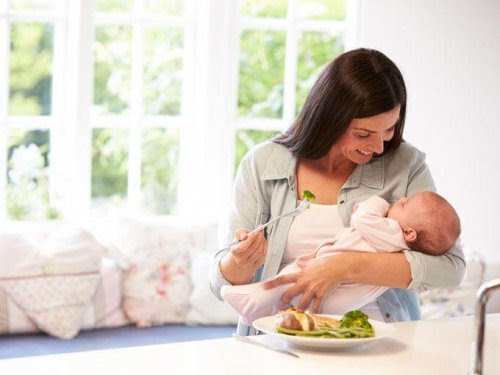 Mamma äter måltid med spädbarn i famnen
