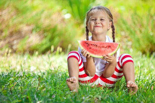 Glad flicka sitter i gräset och äter vattenmelon