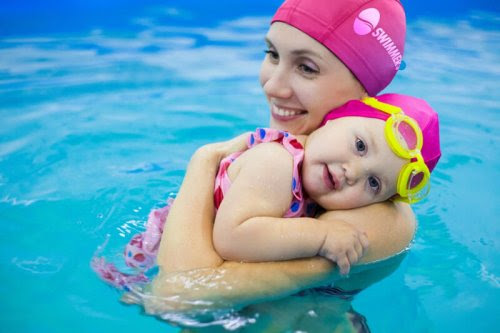 Mamma och bebis i pool med matchande rosa badmössor