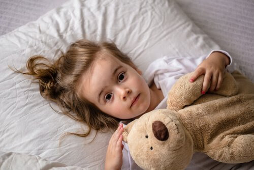 Klarvaken flicka i säng med nalle