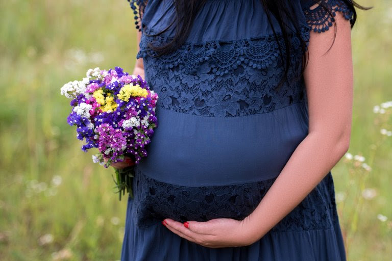 Gravid kvinna i blå klänning med blombukett