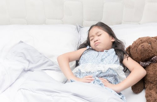 Barn med epilepsi: Orsaker, symtom och behandling: flicka i säng ser plågad ut och håller sig för magen