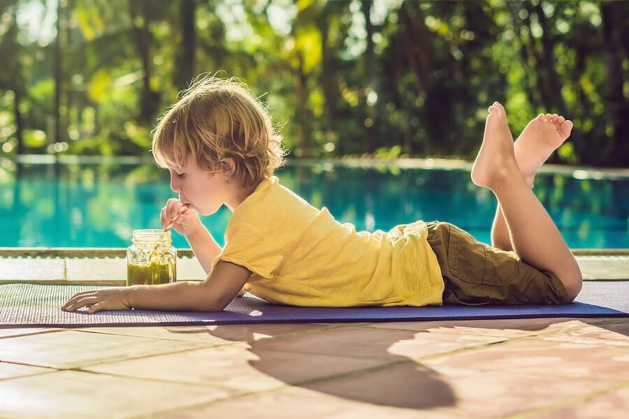 barn ligger på marken framför en pool och dricker grön juice