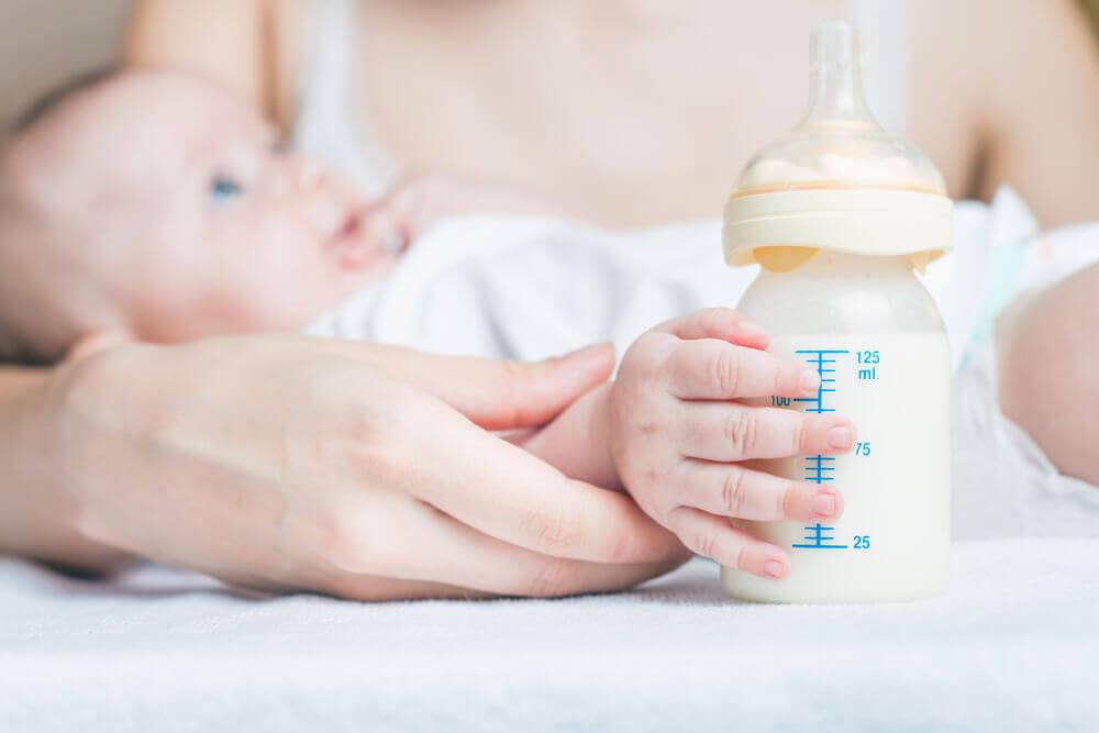 spädbarn i sin mammas famn med nappflaska i förgrunden