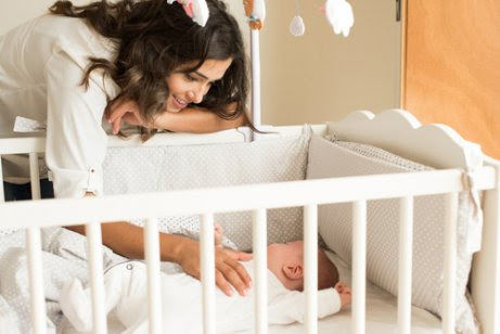 Mamma med bebis i spjälsäng