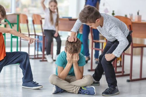 pojke sitter på golvet med händerna för ansiktet, andra barn slår och pekar på honom