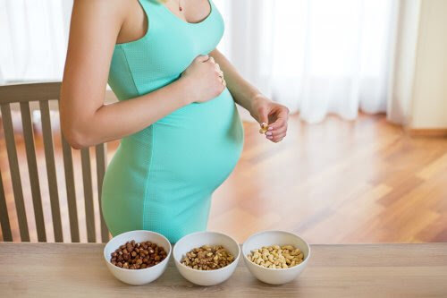 gravid kvinna bredvid bord med tre skålar nötter
