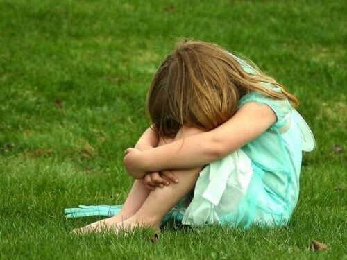 Flicka sitter ihopkrupen på gräs