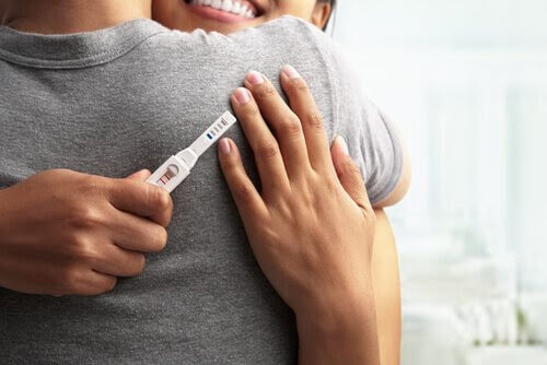 Kvinna och man kramar varandra med ett positivt graviditetstest
