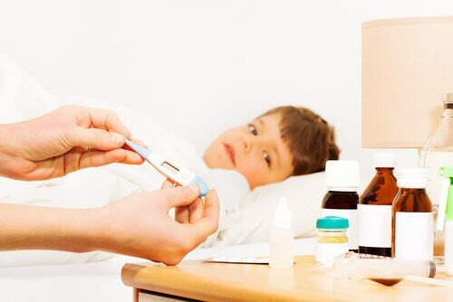 pojke i säng med febertermometer och mediciner i förgrunden
