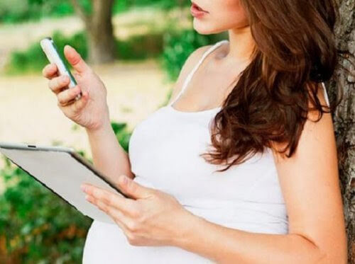 Gravid kvinna med mobiltelefon och läsplatta