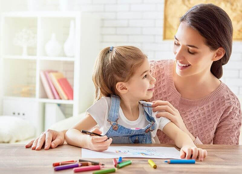 flicka ritar med kritor och mamma tittar på