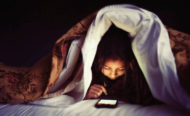 barn med mobiltelefon under täcke