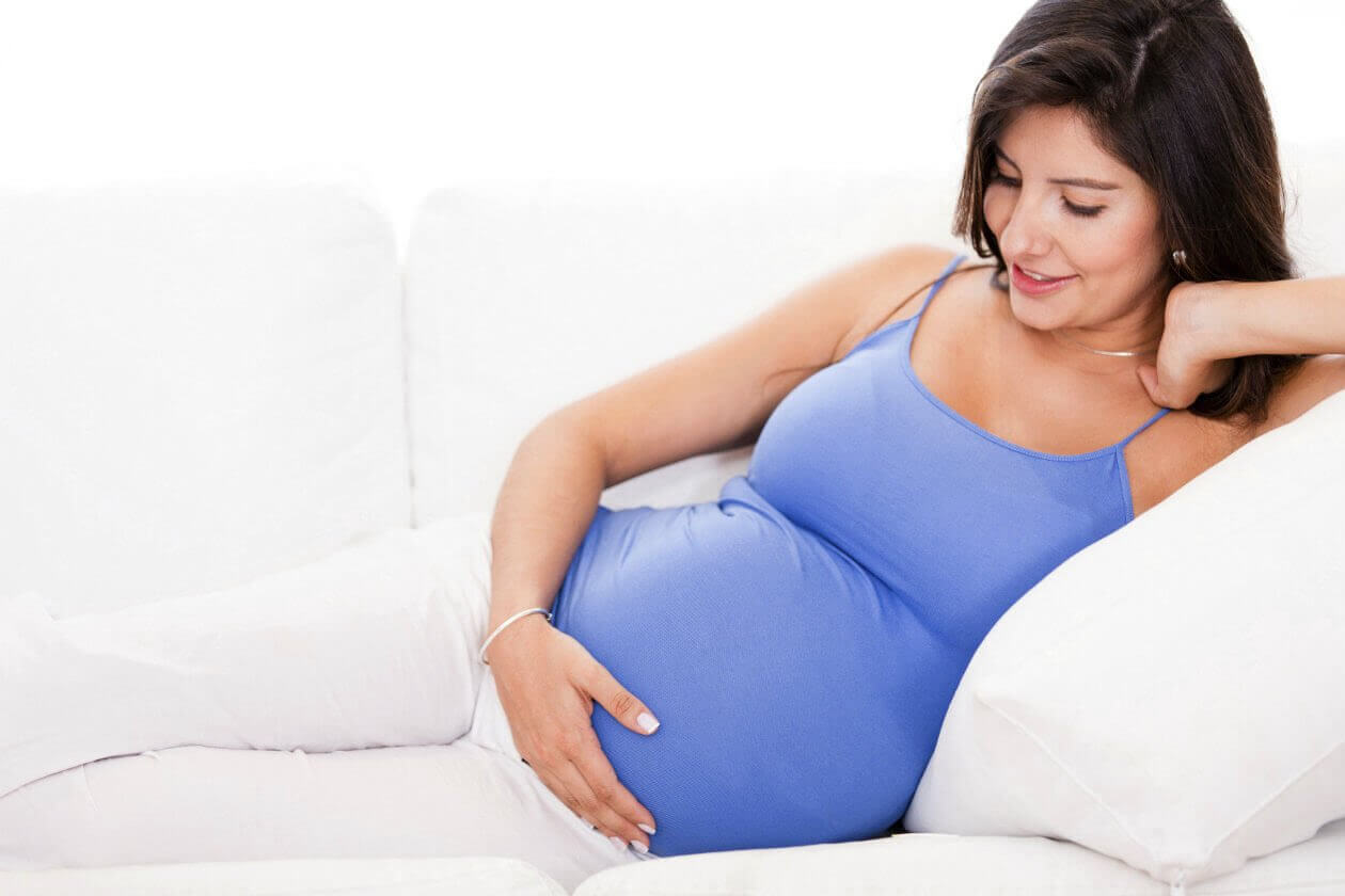 gravid kvinna i soffa med handen om magen