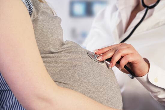 läkare lyssnar på gravid mage med stetoskop