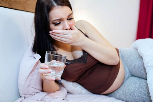 gravid kvinna i säng med ett vattenglas i handen, ser illamående ut