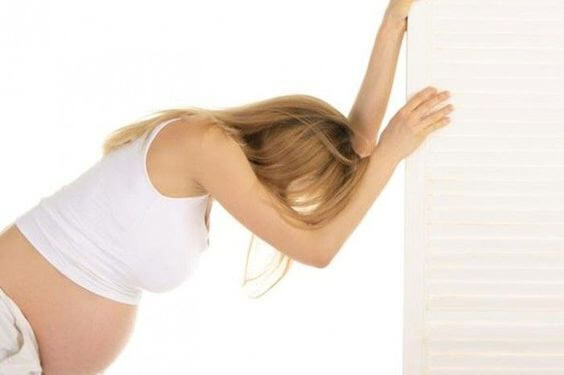 gravid kvinna lutar huvudet mot en vägg