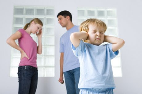 Barn håller för öronen med föräldrar som bråkar i bakgrunden