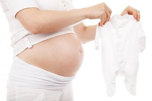 gravid kvinna håller upp babykläder
