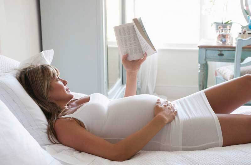 gravid kvinna läser i säng