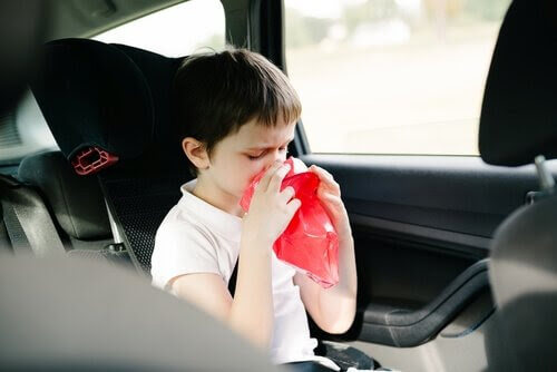 pojke i bil håller kräkpåse framför munnen