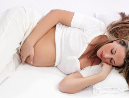 frisk graviditet: gravid kvinna på säng håller sig om mage