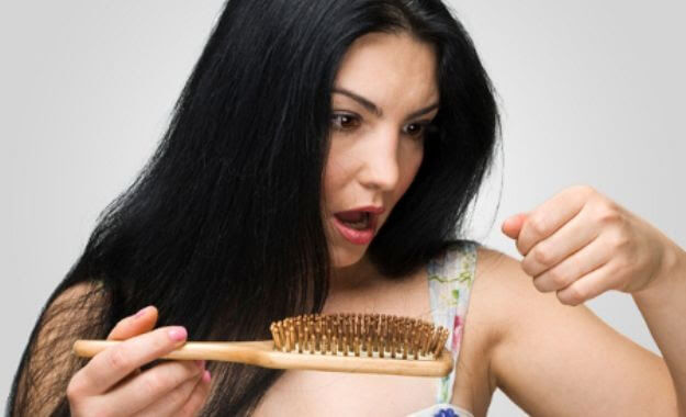 kvinna med hårborste tittar förfärat på tappade hårstrån