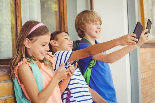 Barn står i rad och tittar på sina smartphones - två tar selfie