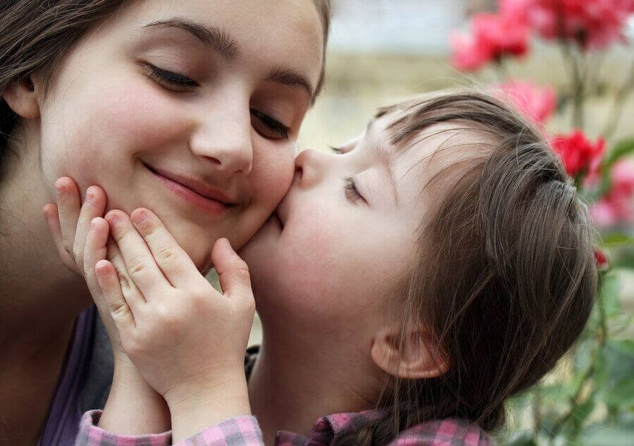 litet barn med downs syndrom kysser kind på äldre syster