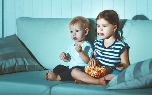 Två små barn i tv-soffa med popcorn