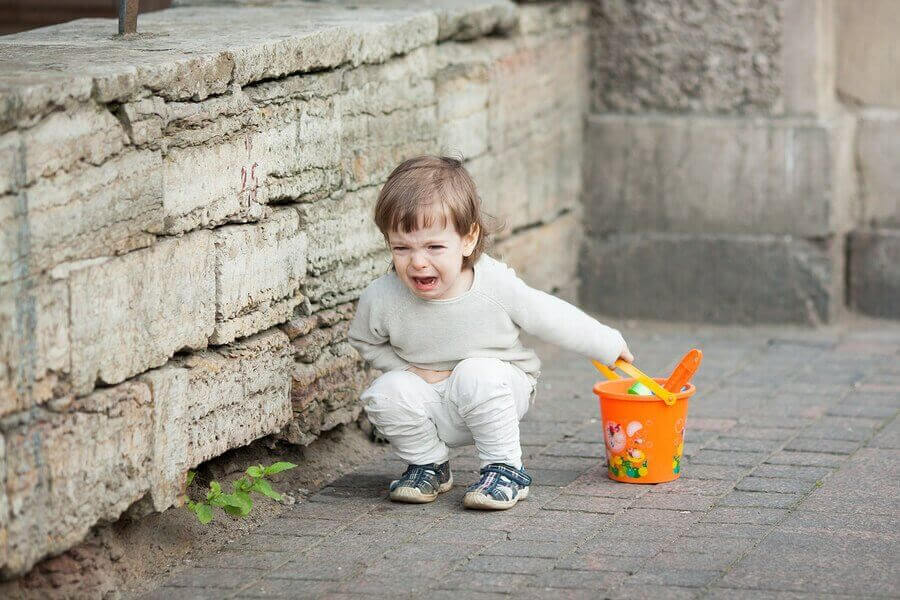 Liten flicka med orange hink sitter och skriker