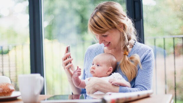 mamma med mobil och baby i knäet