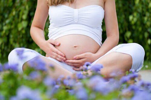 Gravid kvinna sitter utomhus och känner på magen.