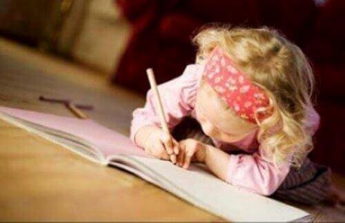 Litet barn använder penna för att skriva i en skrivbok.
