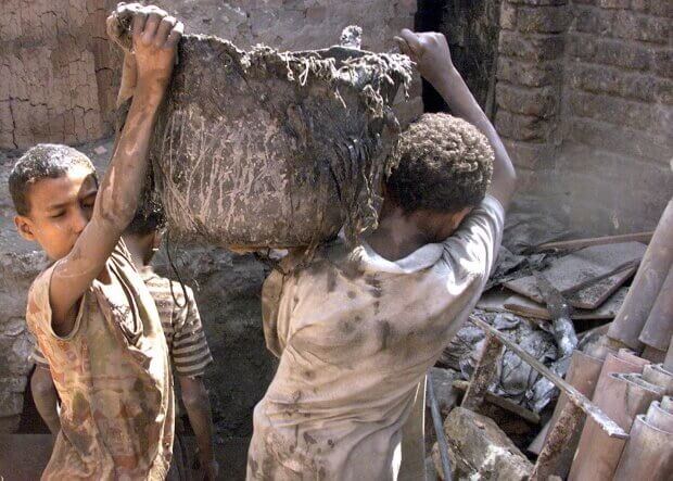 Två barnarbetare som bär en smutsig tunna.