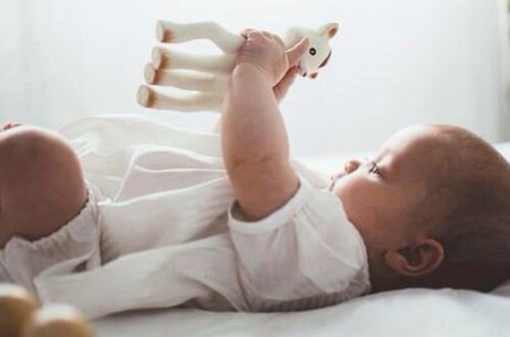 Bebis ligger på rygg och håller i en giraff leksak.