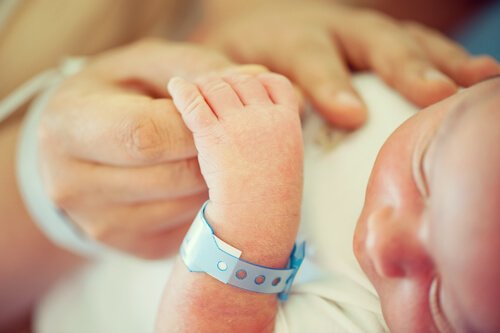 Nyfodd bebis håller i mammans hand.