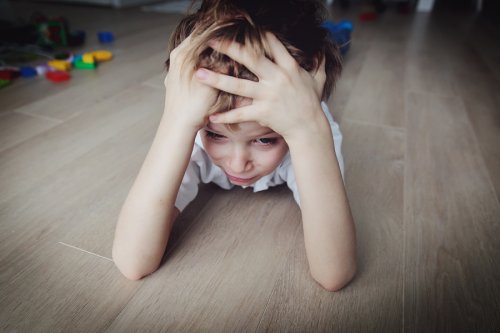 Stressat barn ligger på golvet och håller om sitt huvud.