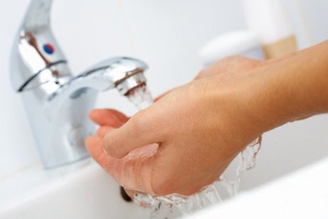 Person som tvättar händerna under vattenkranen.