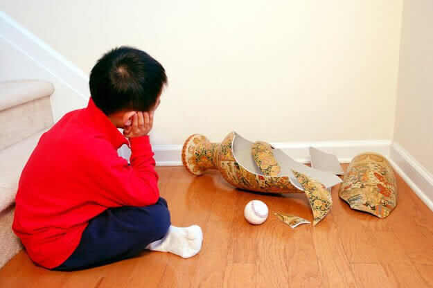 Pojke sitter på golvet bredvid en sönderslagen vas och en boll
