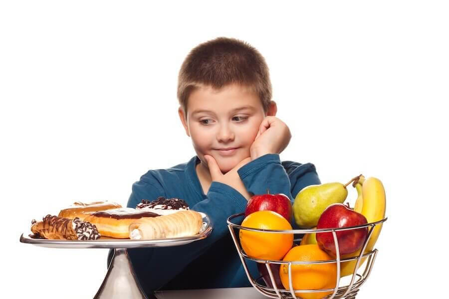 övervikt i barndomen: pojke tittar på bakverk bredvid en skål med frukt