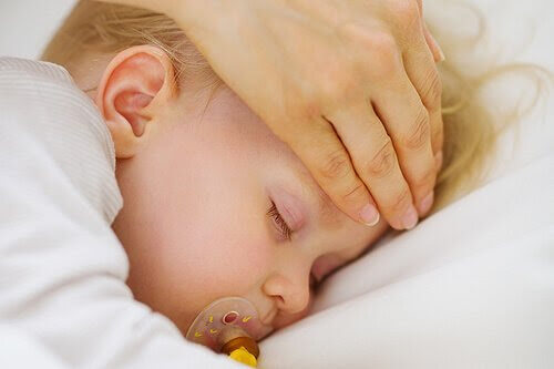 Hand känner på pannan på ett sovande barn