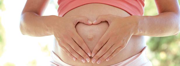 Gravid kvinna håller händerna på magen i form av ett hjärta.