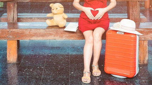 gravid kvinna sitter på bänk med resväska och nalle