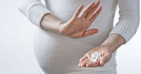 gravid kvinna håller upp en avvisande hand mot piller