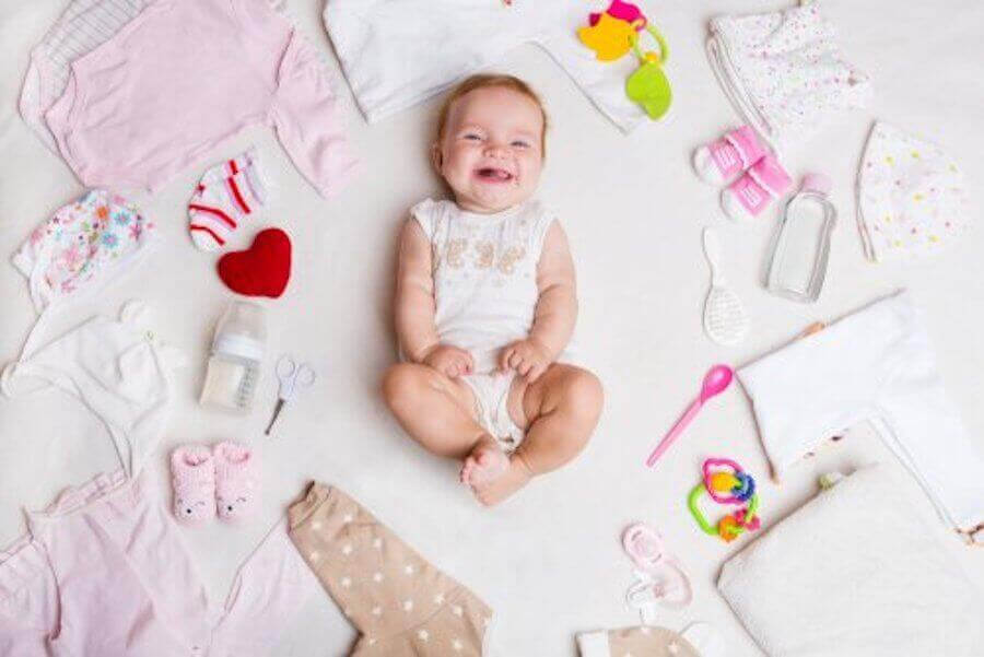 baby omgiven av babykläder och saker